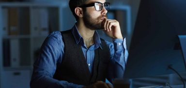 Concentrated entrepreneur or manager sitting by desk in front of computer monitor while working at night