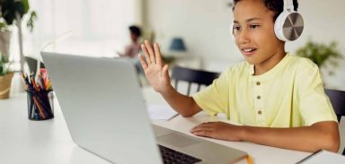 Smiling black boy making video call over laptop and waving while e-learning at home.